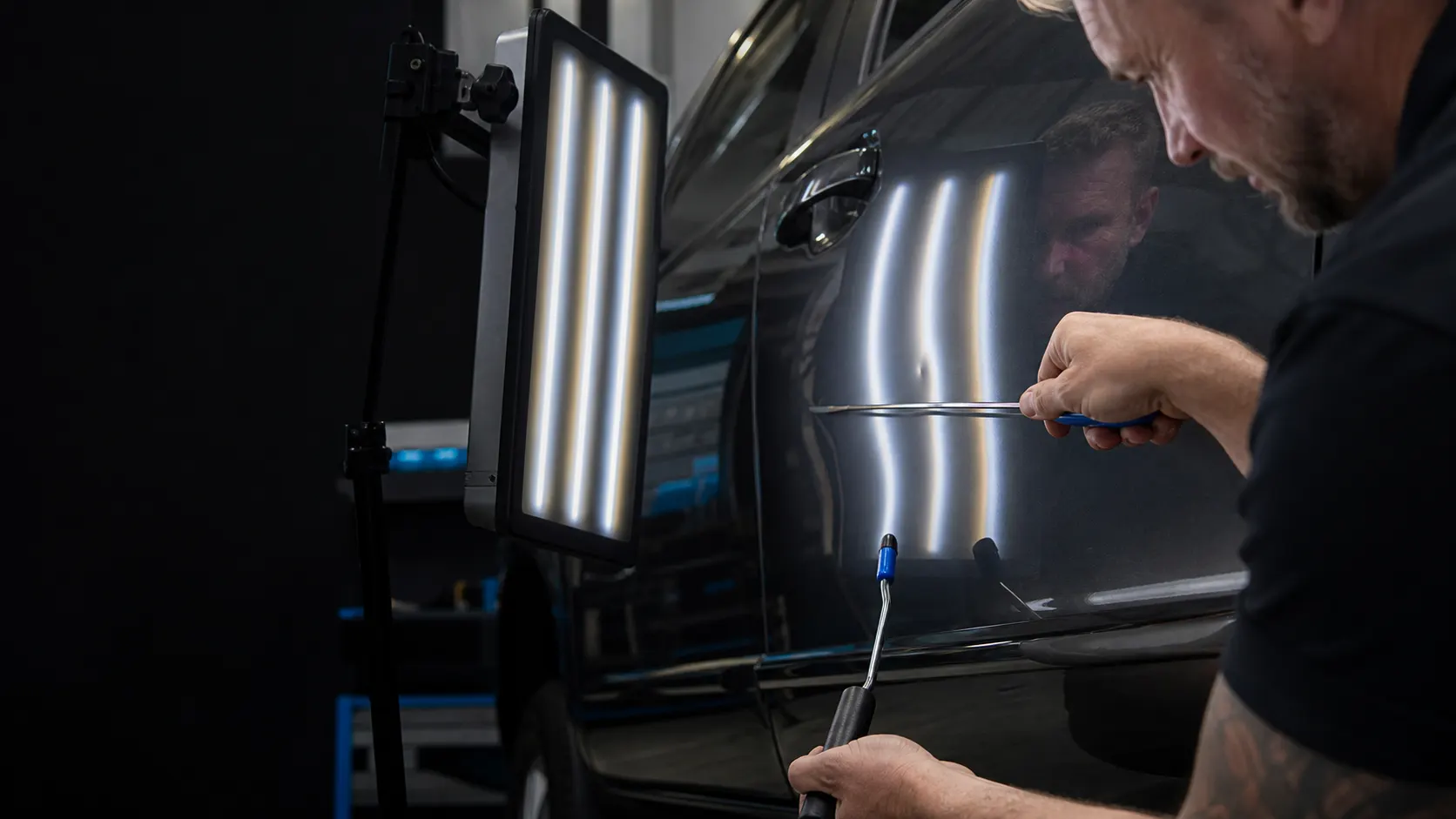 Technician performing precision paintless dent repair on a vehicle door